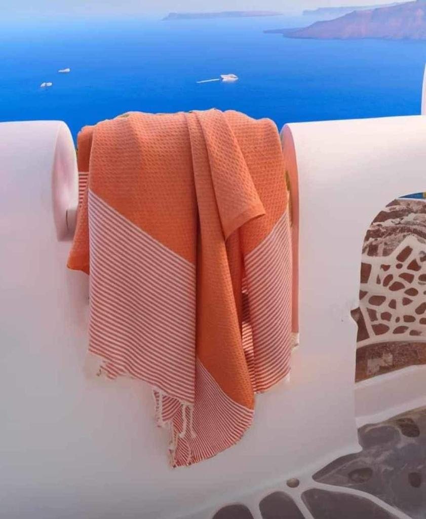 An orange striped fouta draped over a white wall above the blue sea